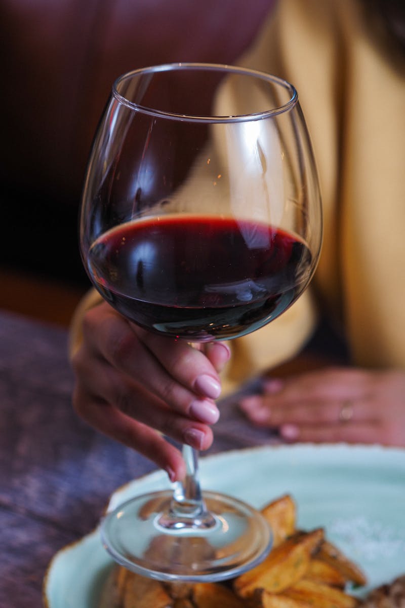 A hand elegantly holding a glass of red wine in a relaxing restaurant ambiance.